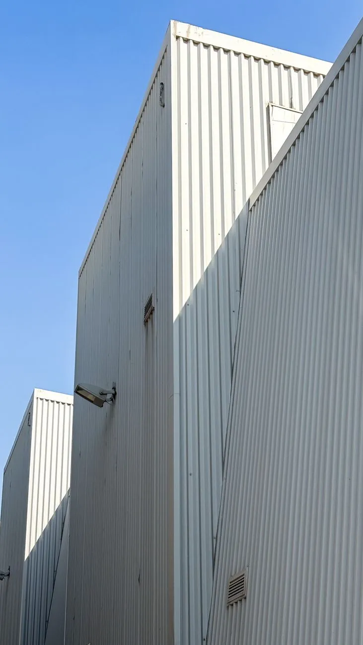 A close-up of a modern industrial building exterior with corrugated metal siding under a clear blue sky.