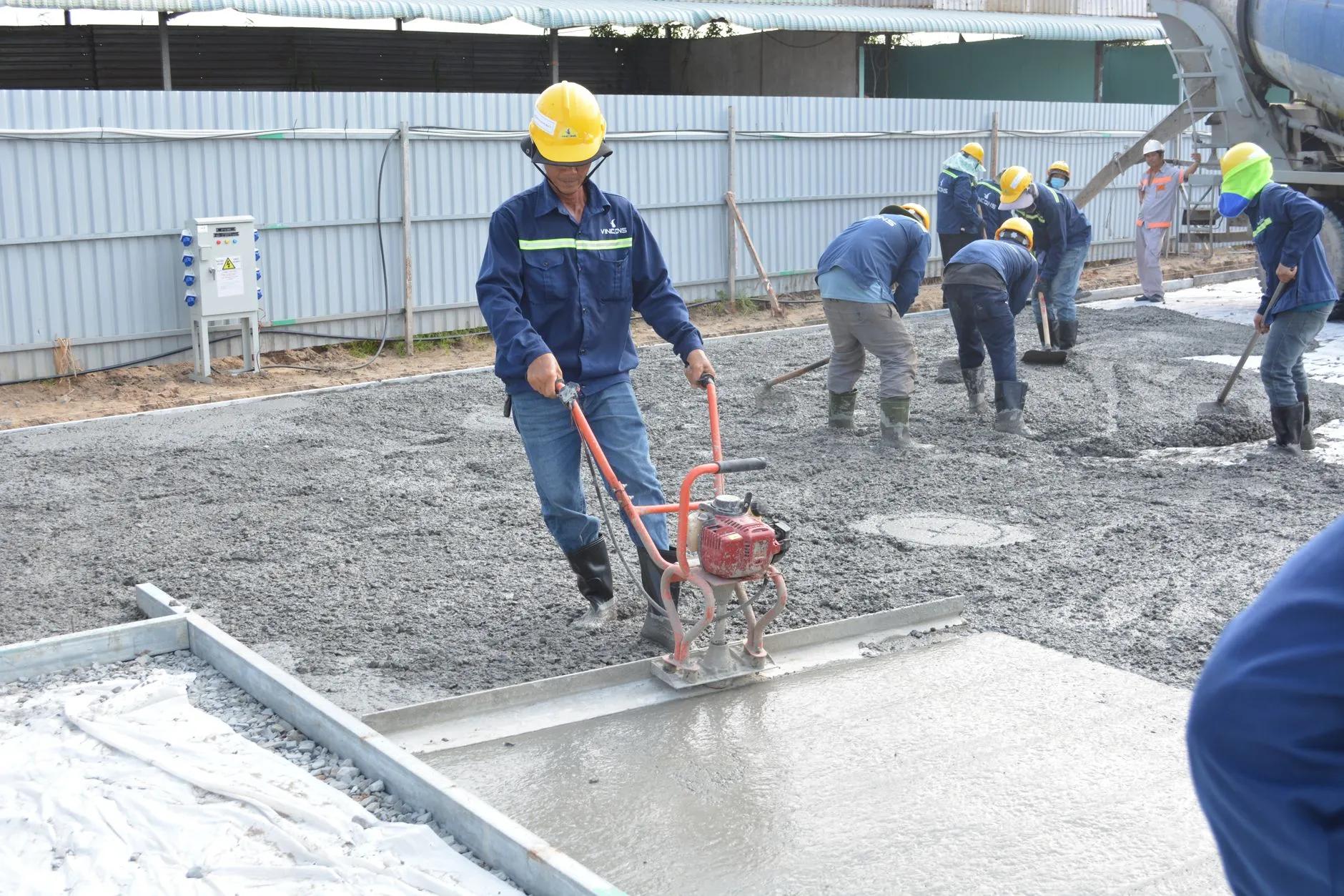 Team of workers smoothing and leveling wet concrete at a construction site.