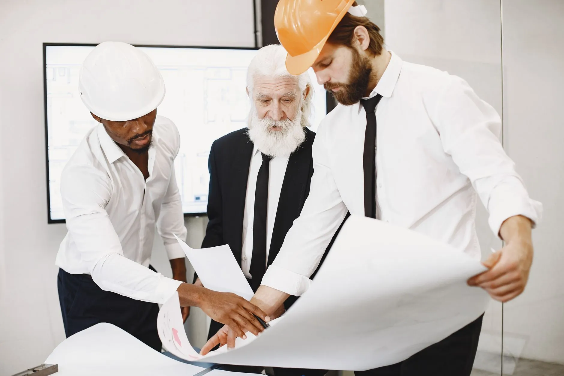 Three architects in office reviewing blueprints, showcasing teamwork and professional attire.